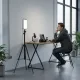 Mini lampe vidéo LED 40W portable avec batterie intégrée et charge PD posée sur un trépied à côté d'un jeune homme assis à un bureau équipé d'un micro, d'un appareil photo et d'un ordinateur portable